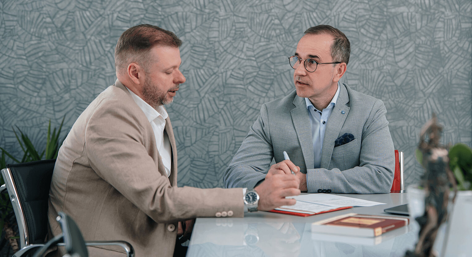 Dr. Nemes Imre ügyvéd egy asztalnál ülve egyeztet egy ügyféllel, előttük az asztalon dokumentumok láthatók. A Dr. Nemes Ügyvédi Iroda szakértelme különösen fontos a cégek jogi védelme és működése szempontjából, figyelembe véve a legújabb jogszabályokat és piaci trendeket.